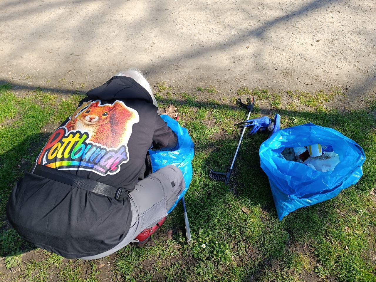 Eine Person mit Pottbundt-Shirt beim Einsammeln von Müll; daneben liegen Greifzange und blaue Müllsäcke
